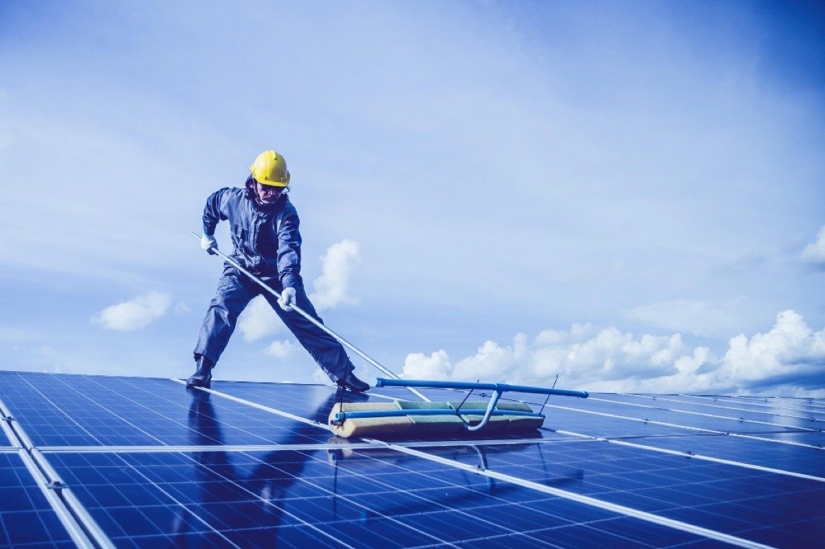 Technicien en casque de sécurité nettoyant des panneaux photovoltaïques avec une brosse télescopique